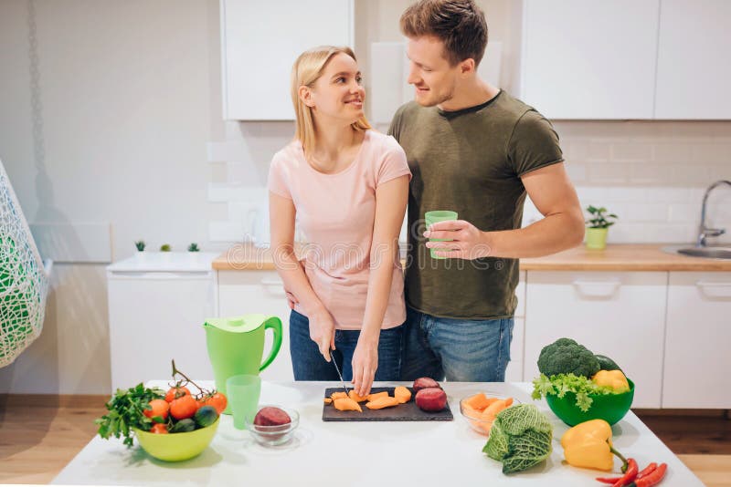 Liebende Familie des strengen Vegetariers, die rohes Gemüse in der Küche kocht Ausschnittgemüse der jungen Frau, während ihr Ehem lizenzfreies stockbild Liebende Familie des strengen Vegetariers, die rohes Gemüse in der Küche kocht Ausschnittgemüse der jungen Frau, während ihr Ehem lizenzfreies stockbild