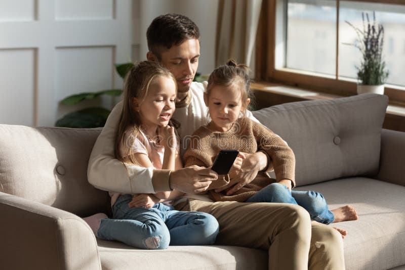 Liebende kleinen Töchter der Vatiumarmung, die Smartphonespielspiele zusammenhalten lizenzfreie stockfotografie