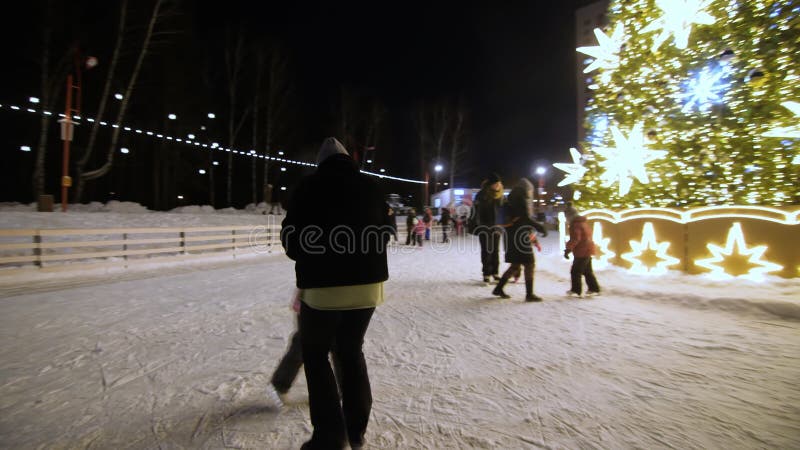 Liebende Mutter lehrt Kinder, auf der Eisbahn am Neujahrbaum Schlittschuhlaufen zu fahren