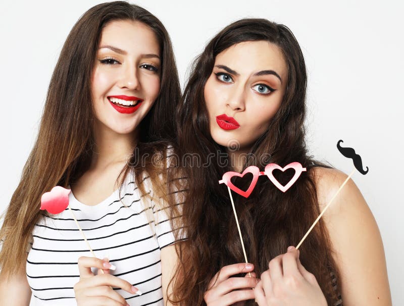 Two stylish girls best friends holding paper party sticks