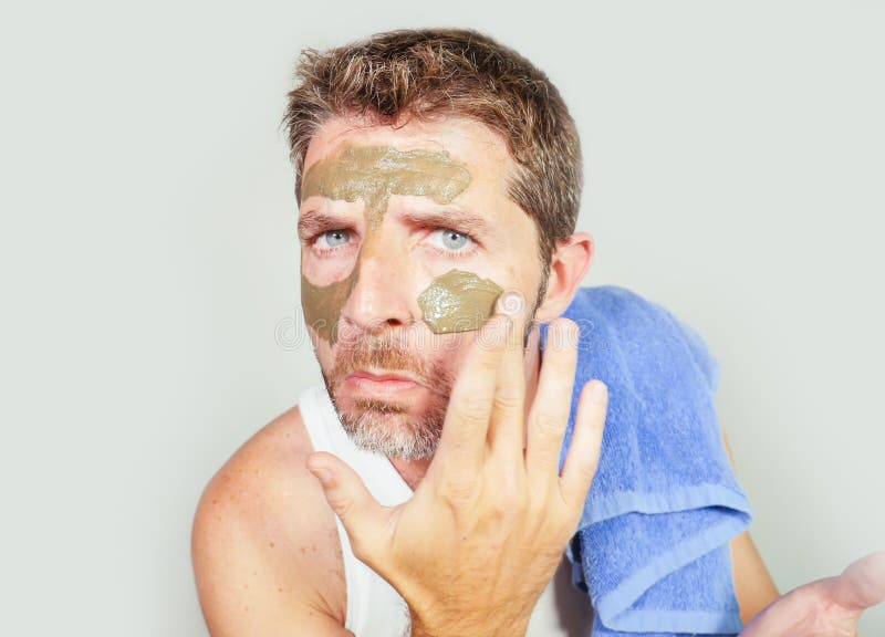 Lifestyle isolated portrait of young attractive and happy man with bathroom towel applying with green cream on his face applying stock photo Lifestyle isolated portrait of young attractive and happy man with bathroom towel applying with green cream on his face applying stock photo