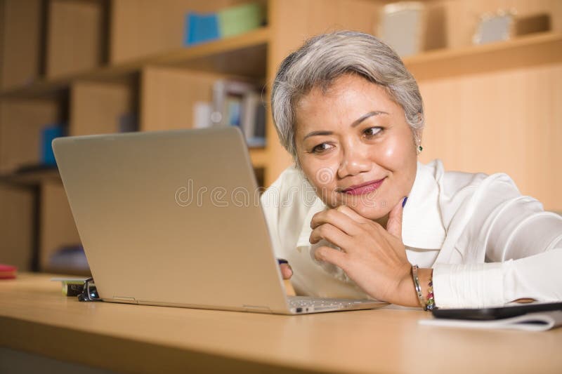 Lifestyle office portrait of attractive and happy successful middle aged Asian woman working at laptop computer desk smiling stock images Lifestyle office portrait of attractive and happy successful middle aged Asian woman working at laptop computer desk smiling stock images