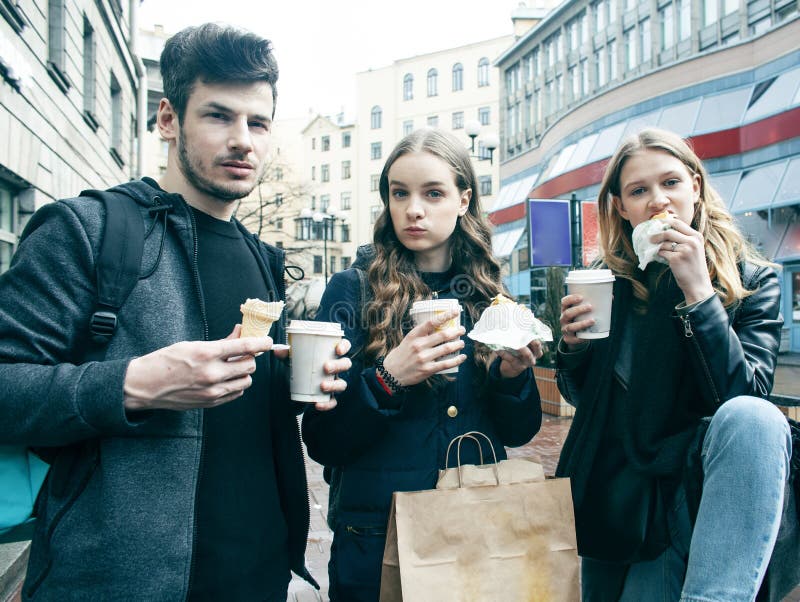 Lifestyle and people concept: two girls and guy eating fast food on city street together having fun, drinking coffee royalty free stock photography Lifestyle and people concept: two girls and guy eating fast food on city street together having fun, drinking coffee royalty free stock photography
