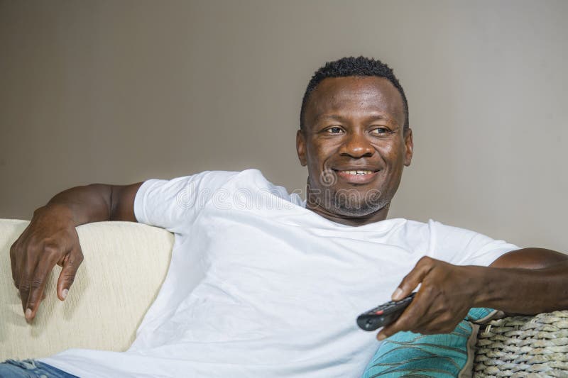 Lifestyle portrait of young attractive and happy black african American man holding TV remote controller watching television movie