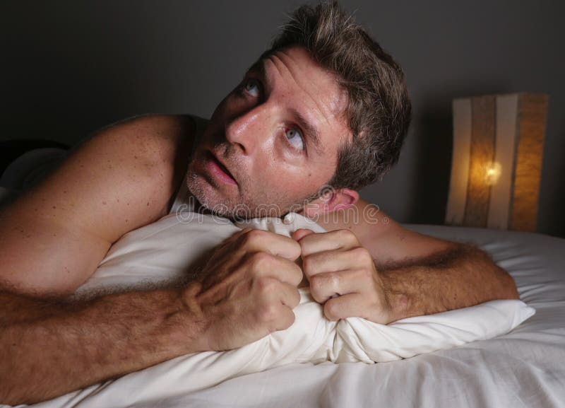 Lifestyle portrait of young attractive scared and paranoid man lying in bed having bad dreams and nightmares looking around in royalty free stock photos