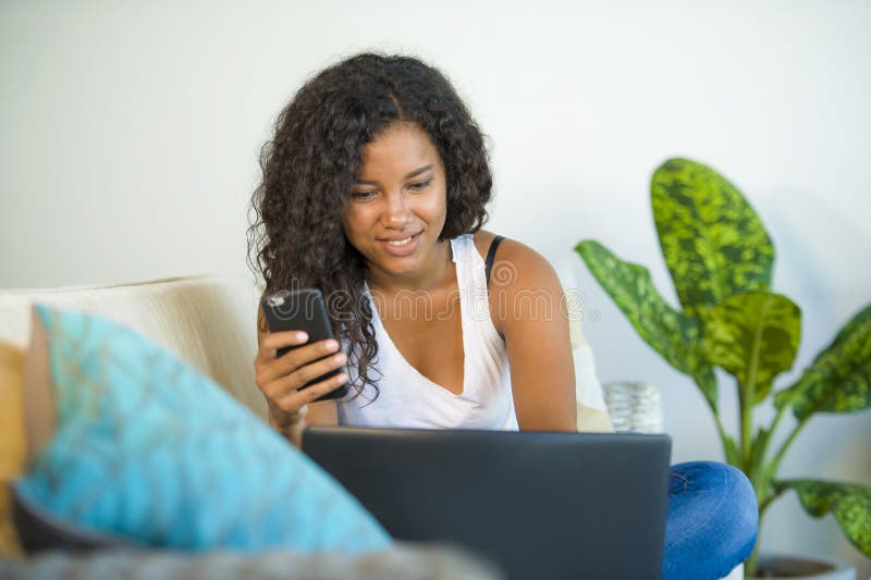 Lifestyle portrait of young happy and beautiful black african American woman using internet mobile phone while working on laptop royalty free stock photos Lifestyle portrait of young happy and beautiful black african American woman using internet mobile phone while working on laptop royalty free stock photos