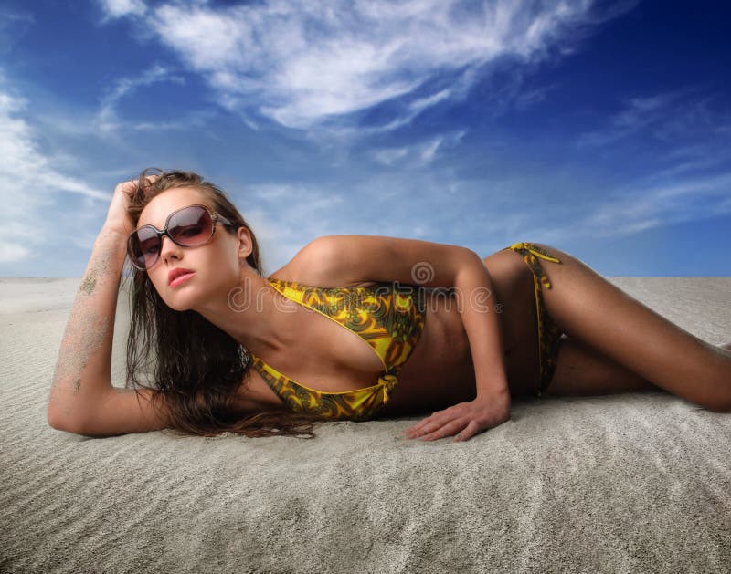 Portrait of a woman in swimsuit and sunglasses lying on the sand. Portrait of a woman in swimsuit and sunglasses lying on the sand