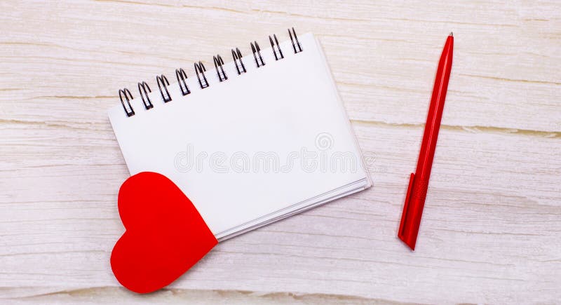 On a light background, a blank notebook, red hearts and a red pen. Place to insert text or illustrations.