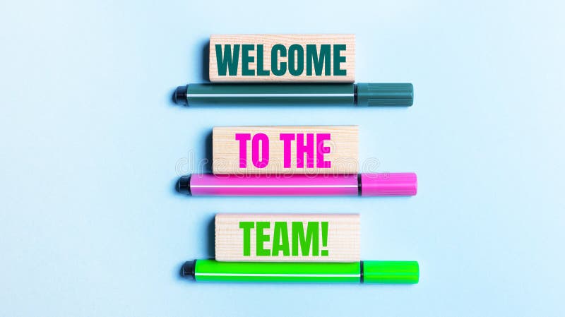 On a light blue background, there are three multi-colored felt-tip pens and wooden blocks with the WELCOME TO THE TEAM stock photos