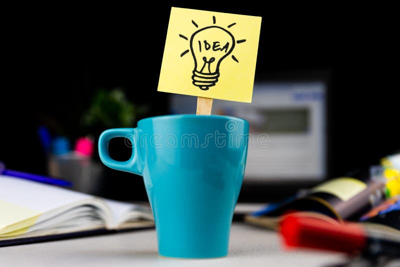 Light bulb doodle drawn on sticky note inside a cup of coffee at the office desk. Ideas, inspiration and creative thinking