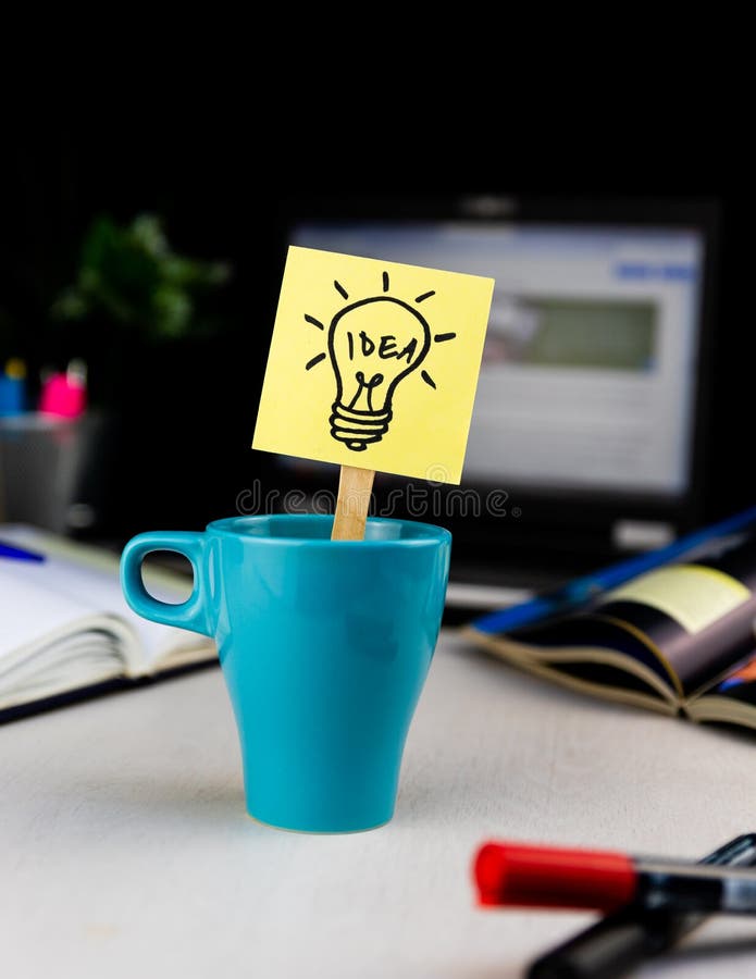 Light bulb doodle drawn on sticky note inside a cup of coffee at the office desk. Ideas, inspiration and creative thinking