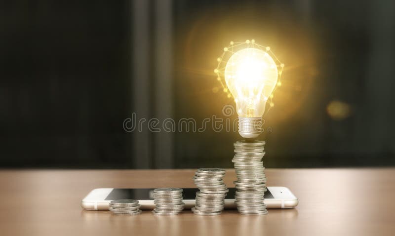 Light bulb on top of coins and smartphone royalty free stock photos