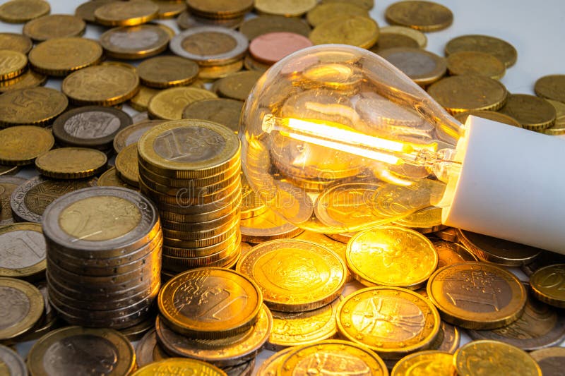 Light bulb turned on, with coins around. Energy costs. stock photos