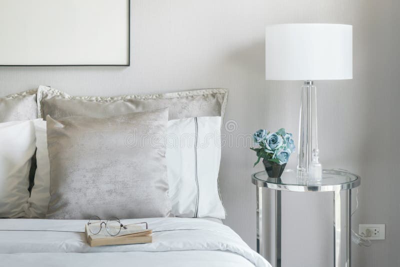 Light Gray and White Pillows on Bed with Flower Jar on Bedside Table