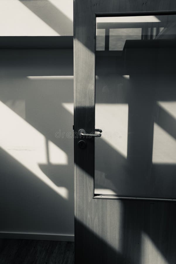 Sun light falling through a window on a wall and door of an office building creating geometrical shadows. Sun light falling through a window on a wall and door of an office building creating geometrical shadows