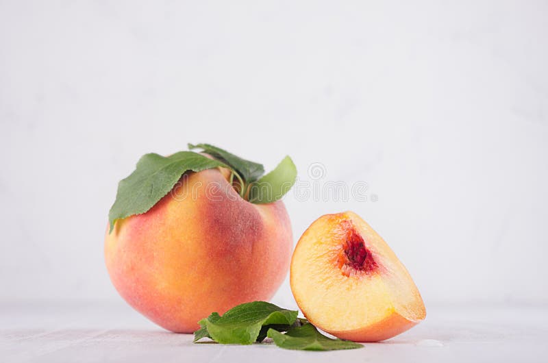 Light soft summer fruit background - ripe peach with bright fresh piece and green leaf on white wood table, copy space.