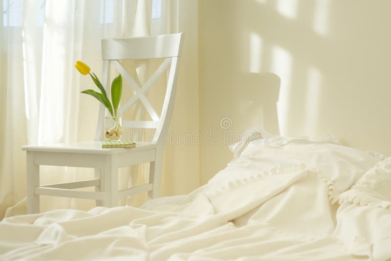 Light spring bedroom interior, bed, white chair, glass with yellow tulip, window light curtains, pastel colors