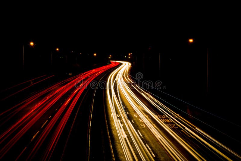 Light trails from moving car headlights and rear vehicle lights creating moving blurred motion at night