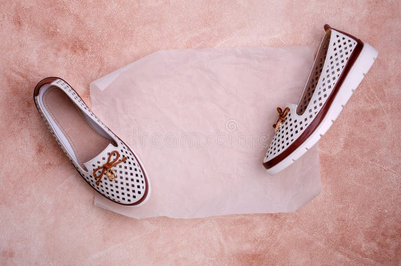 Light women`s shoes with a bow and perforation on a brown background. Design concept. A copy of the space. Selective focus