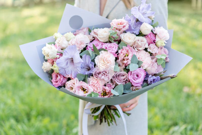 Lila und rosa schöner Frühlingspastellblumenstrauß Junges Mädchen, das eine Blumenanordnung mit verschiedenen Blumen hält hell stockfotografie