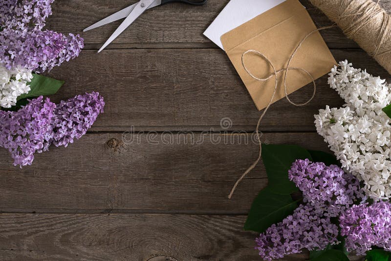 Lilac blossom on rustic wooden background with empty space for greeting message. Scissors, thread reel, small envelope