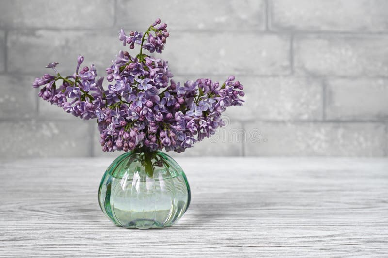 Lilac Flowers in Vase on a Table Against Grey Brick Wall Stock Photo