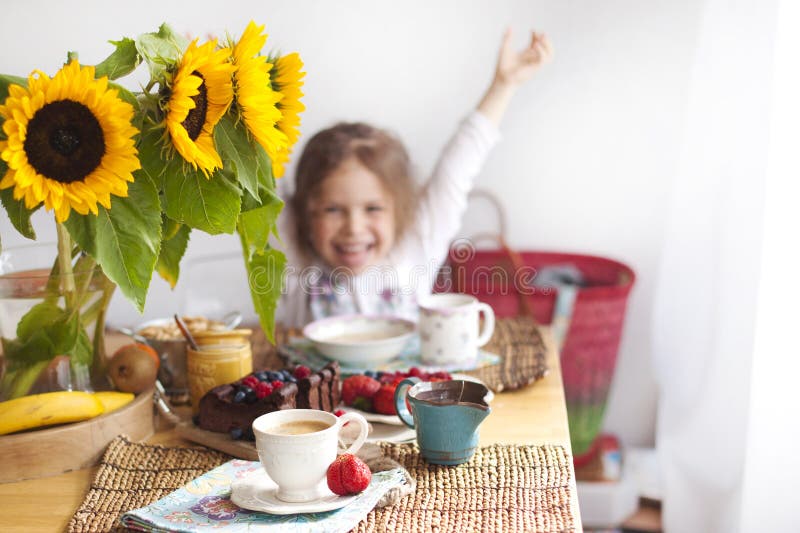 Lilla flickan har frukosten hemma På tabellen är en bukett av blommor av solrosor och en söt paj med frukt, fotografering för bildbyråer Lilla flickan har frukosten hemma På tabellen är en bukett av blommor av solrosor och en söt paj med frukt, fotografering för bildbyråer