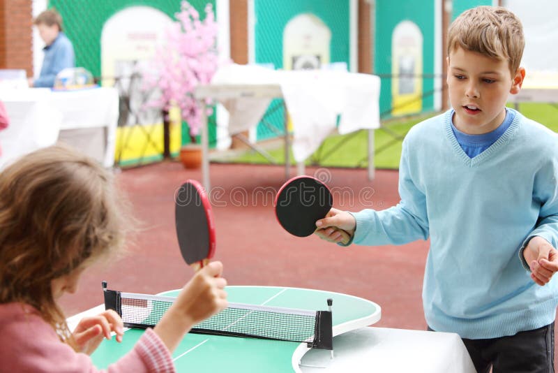 Lilla flickan och pojken i blått spelar bordtennis parkerar in arkivfoto Lilla flickan och pojken i blått spelar bordtennis parkerar in arkivfoto