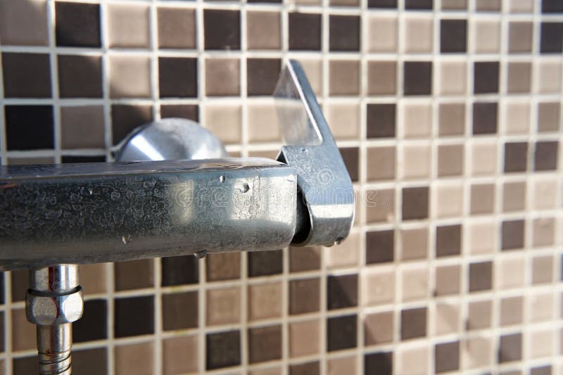 Limescale on the dirty faucet switch in the shower room. Brown tiles on the wall stock photography