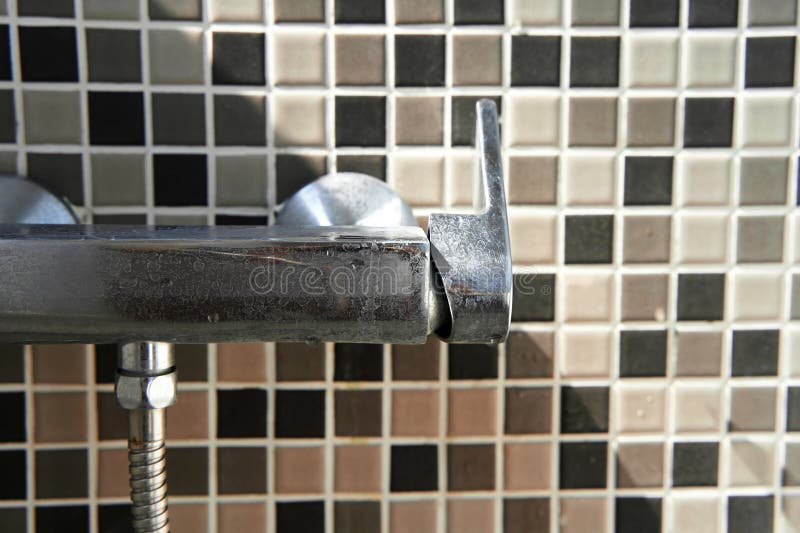 Limescale on the dirty faucet switch in the shower room. Brown tiles on the wall royalty free stock images
