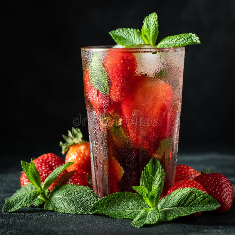 Limonata fresca con ghiaccio, la menta e la fragola sulla cima in vetro sul fondo nero della tavola Bevanda fredda di estate Vetr fotografia stock Limonata fresca con ghiaccio, la menta e la fragola sulla cima in vetro sul fondo nero della tavola Bevanda fredda di estate Vetr fotografia stock