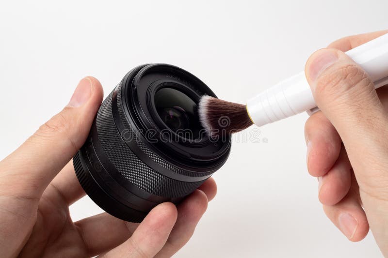 Cleaning digital camera lens, hands cleaning dust from front of lens with a special cleaning pencil, blurred background with lenses on the white surface. Close up. Cleaning digital camera lens, hands cleaning dust from front of lens with a special cleaning pencil, blurred background with lenses on the white surface. Close up.