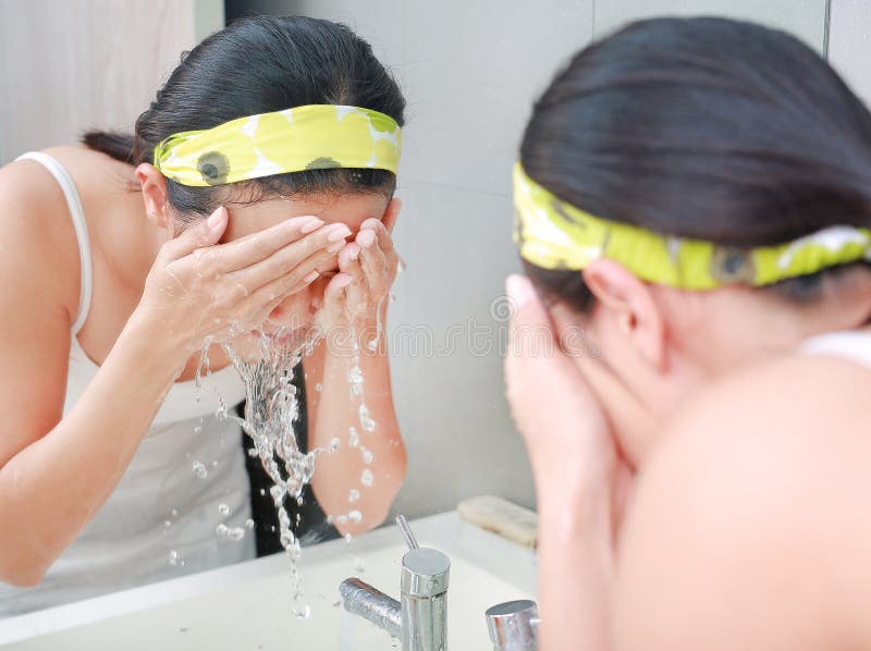 A limpeza da mulher que lava sua cara reflete com espelho do banheiro foto de stock A limpeza da mulher que lava sua cara reflete com espelho do banheiro foto de stock