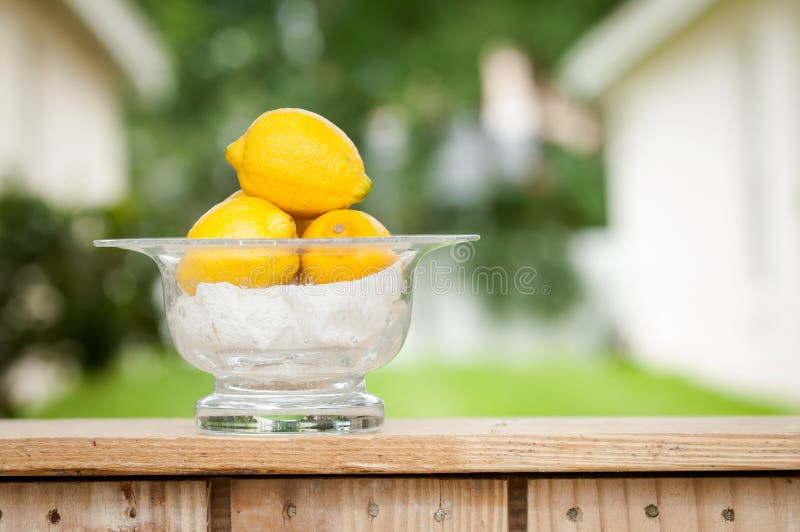 A glass bowl of lemons sitting on the counter of an outdoor lemonade stand. A glass bowl of lemons sitting on the counter of an outdoor lemonade stand.