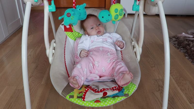 Linda bebé tendida en una silla de rebotador y mirando juguetes. la bebé tiene 2 meses