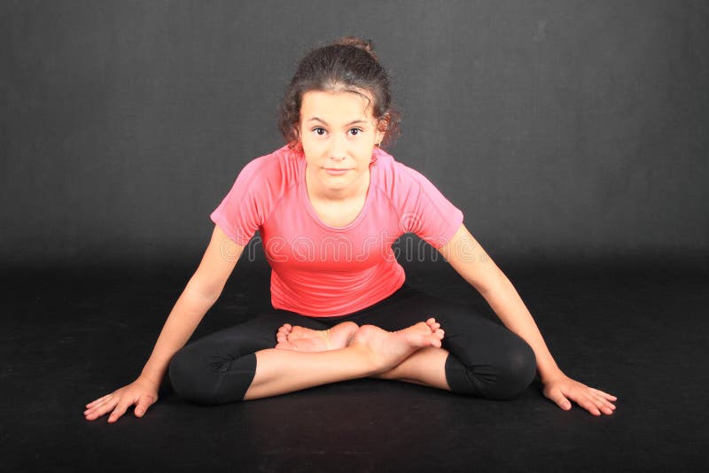 Pretty girl - barefoot brunette schoolkid dressed in pink t-shirt and black leggings, exercising yoga pose lotus pose or padmasana. Active childhood concept. Pretty girl - barefoot brunette schoolkid dressed in pink t-shirt and black leggings, exercising yoga pose lotus pose or padmasana. Active childhood concept.