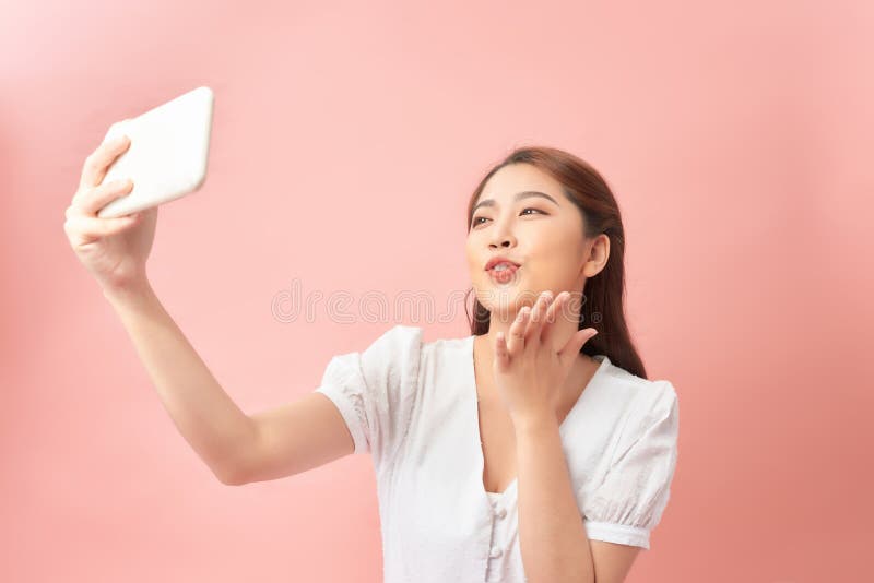 Linda e divertida jovem tirando selfie com telefone celular sobre fundo rosa fotografia de stock royalty free