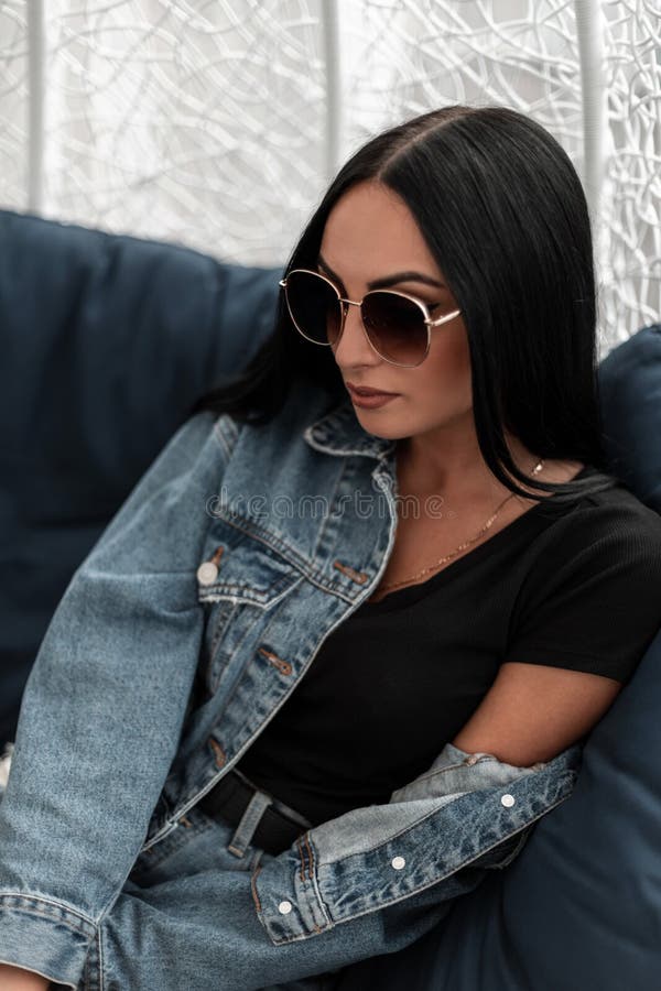 Linda e sexy jovem morena em uma jaqueta elegante em uma camiseta em óculos de sol da moda gosta de relaxar sentada em uma camisa foto de stock Linda e sexy jovem morena em uma jaqueta elegante em uma camiseta em óculos de sol da moda gosta de relaxar sentada em uma camisa foto de stock