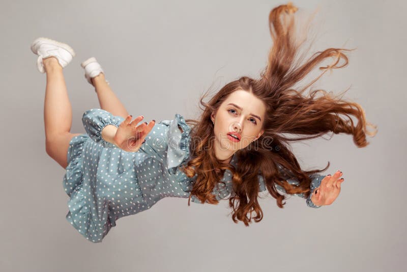 Beautiful girl levitating in mid-air, falling down and her hair messed up soaring from wind, model flying hovering with dreamy peaceful expression. indoor studio shot isolated on gray background. Beautiful girl levitating in mid-air, falling down and her hair messed up soaring from wind, model flying hovering with dreamy peaceful expression. indoor studio shot isolated on gray background