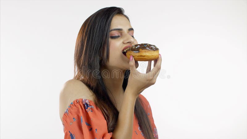 Linda menina indiana comendo rosquinhas de chocolate iummy isoladas sobre fundo branco