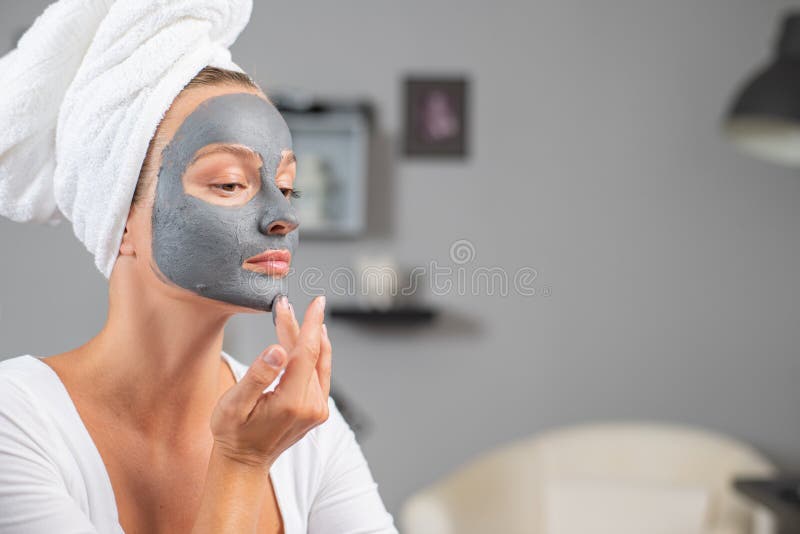 A linda mulher está aplicando máscara de barro facial. Tratamentos da beleza e do céu foto de stock royalty free A linda mulher está aplicando máscara de barro facial. Tratamentos da beleza e do céu foto de stock royalty free