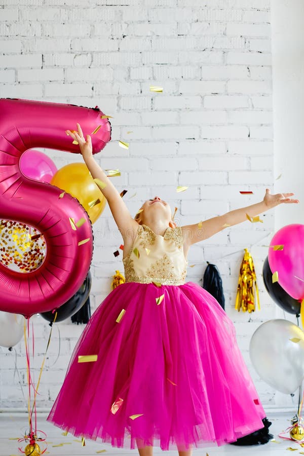 Linda niña de 5-6 años con elegante vestido rosa sobre fondo gris. mirando  a la cámara fiesta de cumpleaños. celebracion.
