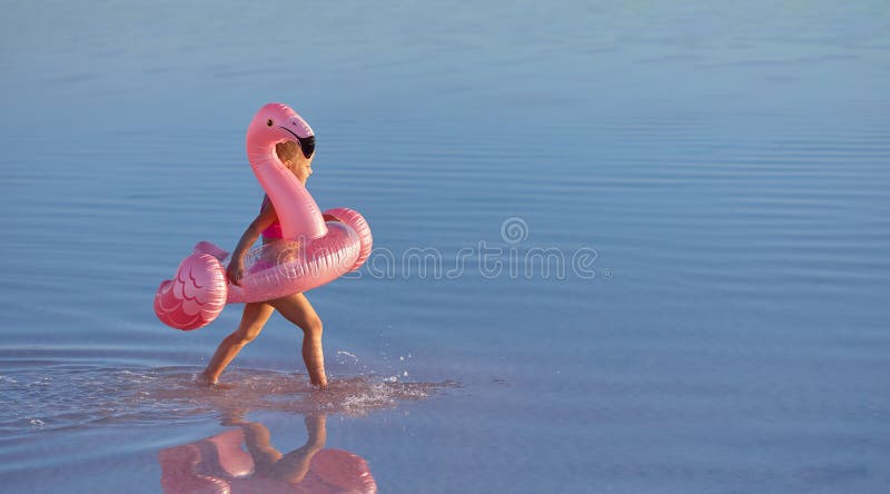 Linda Niña Pequeña Con Traje De Baño Rosa Que Con Flamencos Rosados Inflables En La Playa. Color Azul Del Agua En El Foto de archivo - Imagen de inflable, poco: