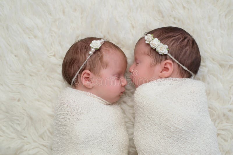 Profile headshot of two fraternal twin newborn baby girls sleeping and swaddled in white. Profile headshot of two fraternal twin newborn baby girls sleeping and swaddled in white.