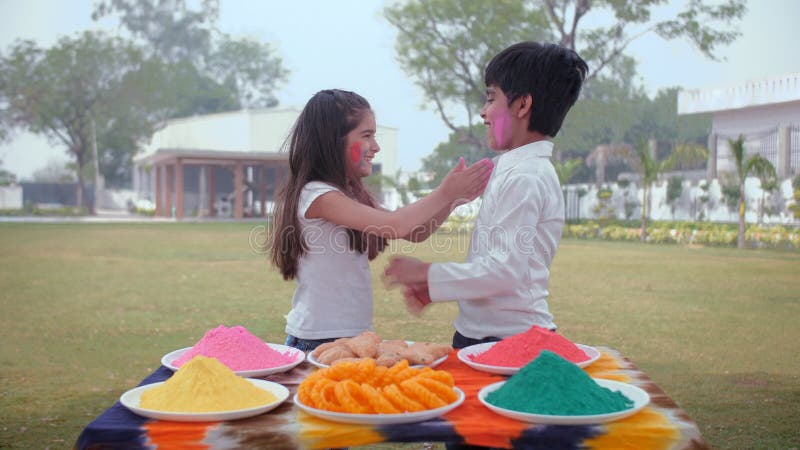 Lindo chico indio y una niña pequeña aplicando el color del polvo unos a otros mejillas gulal orgánico un festival de primavera. almacen de metraje de vídeo