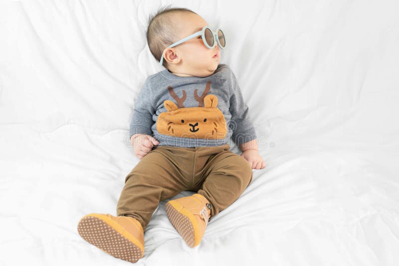 Lindo 4 Meses Niño Pequeño Asiático Vestido Con Ropa Elegante Usa Gafas Y Botas Bebé Sentados En Una Manta Blanca Fría Y Felizm Imagen archivo - Imagen cama, bebé: