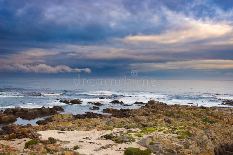 Linea rocciosa della costa sull'oceano a De Kelders, Sudafrica, famoso per la sorveglianza della balena Cielo nuvoloso e drammati fotografia stock libera da diritti Linea rocciosa della costa sull'oceano a De Kelders, Sudafrica, famoso per la sorveglianza della balena Cielo nuvoloso e drammati fotografia stock libera da diritti