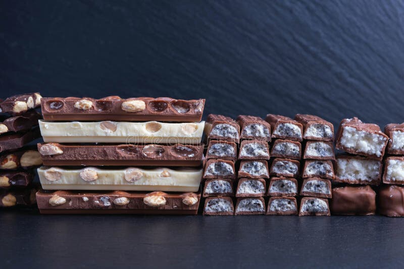 Lined in a row different chocolate bars with nuts and coconut on a black background