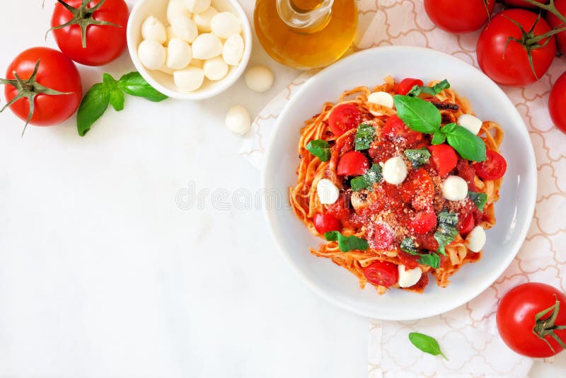 Linguine makaron z pomidorami, mozzarellą i basilem, odgórnego widoku kąta granica nad bielu marmurem fotografia stock Linguine makaron z pomidorami, mozzarellą i basilem, odgórnego widoku kąta granica nad bielu marmurem fotografia stock