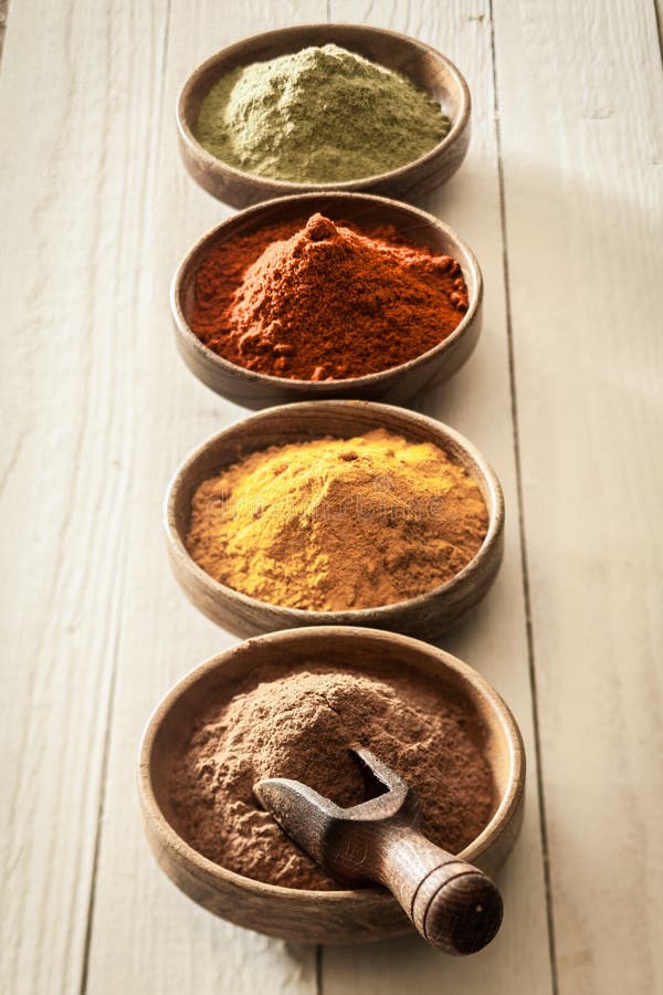 Receding line of colourful spices with curry, chilli or red pepper, cinnamon and matcha powder in small bowls on a background of white painted boards. Receding line of colourful spices with curry, chilli or red pepper, cinnamon and matcha powder in small bowls on a background of white painted boards